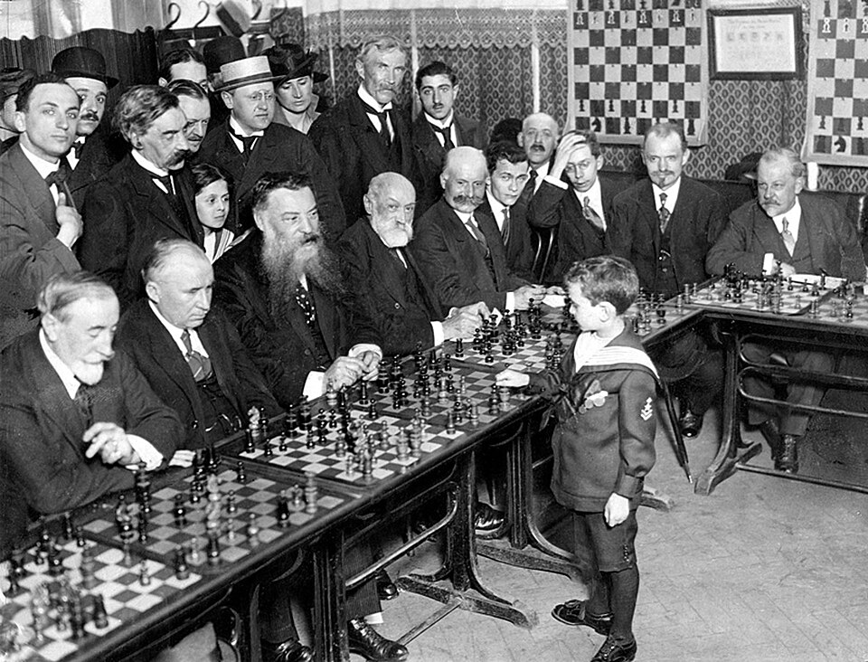 The chess prodigy Samuel Reshevsky, 8 years old, performing a simultaneous exhibition against adults in Paris, 1920.